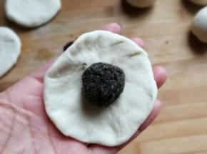 取一份醒发好的面团，用手压成中间厚四周薄的面片，再放上一份豆沙馅儿，包起来然后搓圆