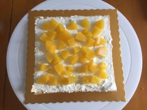 蛋糕片放在转盘上，抹上一层奶油，撒上黄桃颗粒