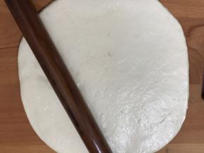 把醒好的面团，用擀面杖擀成披萨盘大一圈的面皮