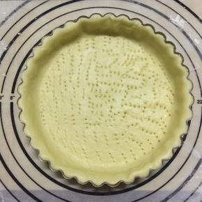 10、把面块放入派盘中，抖动几下使面块贴住派盘，再用手指轻压使面片紧贴派盘，去除边缘，用叉子扎孔