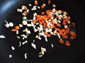 锅内放油烧热，放入胡萝卜丁和蘑菇丁，翻炒半分钟