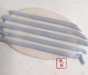 切出两个3克白面团，分别擀成薄片，蓝色面团擀薄切成细面条排在白面片上，用擀面杖轻压再擀开。