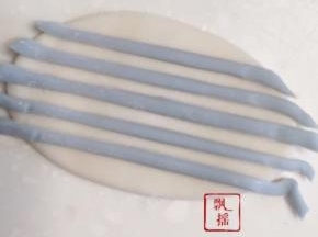 切出两个3克白面团，分别擀成薄片，蓝色面团擀薄切成细面条排在白面片上，用擀面杖轻压再擀开。