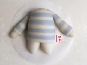 搓两个2克白面团，搓水滴后，另一片条纹面片对半切开，同样的方法包住水滴，置于身体两侧