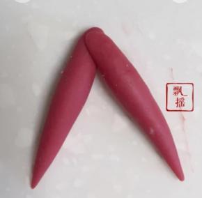 剩下红色面团一分为二，搓成梭型，整成倒V