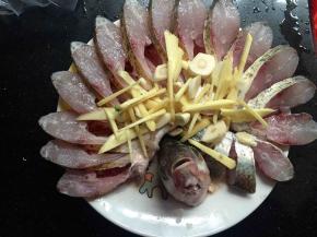 把切好的葱姜蒜放在摆好的鱼身上，加入一勺料酒，大概2.5克左右的盐，1克左右的糖均匀的撒在开屏的地方，腌制10分钟左右，腌制是为了更好的入味，你要是急着烧可以时间短一点