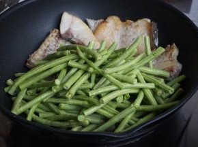 豆角倒入，将豆角翻至锅底，鱼肉放豆角上面。加入适量水、酱油、一丁点糖、一匙蚝油、盐（盐不要放太多，因为鱼肉已经用盐腌过）