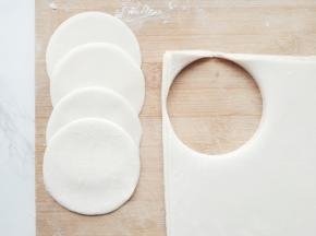 将压好的面片折叠，再用圆形模具压出饺子皮，边角料可以团在一起再压成面片再操作。