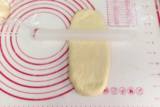 取一份松弛好的面团，用手拍扁，用擀面杖把面团擀成椭圆形。