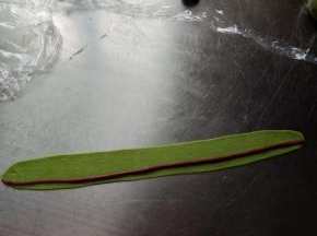 用同样的方法来做青蛙的脸颊，取一个红色的面团搓长，取一个18克的绿色面团擀长包裹住红色的面团，做好两个保鲜膜盖好备用