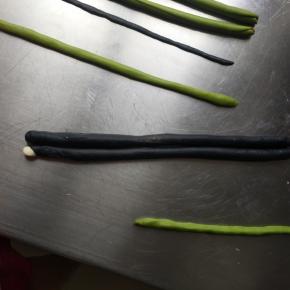 开始整形，两只眼睛摆好，眼镜中间放上刚才的绿色三角形，倒着放，两边再摆上刚才做好的脸颊，2克的黑色面团搓长稍微按扁做嘴巴然后再放一条绿色面团，6克的黑色面团擀成长方形盖在脸颊的上面，