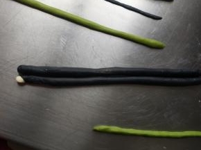 开始整形，两只眼睛摆好，眼镜中间放上刚才的绿色三角形，倒着放，两边再摆上刚才做好的脸颊，2克的黑色面团搓长稍微按扁做嘴巴然后再放一条绿色面团，6克的黑色面团擀成长方形盖在脸颊的上面，