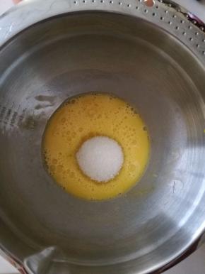 用手动打蛋器将鸡蛋打散，放入全部的白砂糖，搅拌至糖融化。