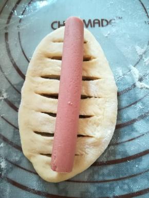 翻面，用锋利的小刀在面团的中间划开几道裂口，放入一根香肠，捏紧收口