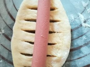 翻面，用锋利的小刀在面团的中间划开几道裂口，放入一根香肠，捏紧收口