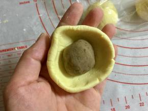 把糯米团在手里按一下，转着边缘捏出碗状，把栗子馅团包进去。
