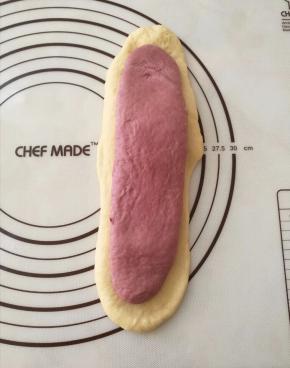 拿一个白色面团，擀成椭圆长条形，宽度不要超过吐司盒的宽度，紫色面团擀成比白色小一圈的长条形。紫面团放在白色面团上。