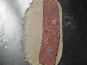 擀成椭圆形一边用手压平底边如图，放一片培根，放整条的，我是因为家里没有整条的培根。边上留1-2cm的空隙，撒少许黑胡椒，从一边卷起，收口向下排入烤盘。