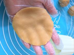 取一个面团，用手掌根部压成能包裹住豆沙蛋黄馅一半量的大小
