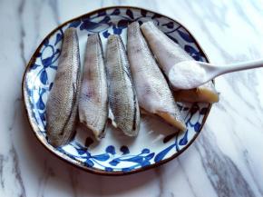 将处理好的南极冰鱼段放入器具中，加入食用盐，用手轻轻按摩。