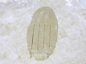 取一个面团，压扁，用擀面杖擀成椭圆形，下端用手指压扁，偏下的位置用刀划出四道口。