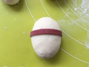 红色面团用擀面杖擀成薄片，用刀分切成0.5厘米宽的条，取一条沾点水，围在白色面团的三分之一处