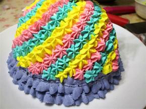 12.	再分别取适量淡奶油，分别加入蓝色，黄色，粉色色素，然后用星星裱花嘴挤到裙子上，最后用绿色调好淡奶油，裱花袋剪一点点小口，挤在娃娃的身上，芭比娃娃蛋糕完成了。