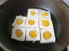 然后再把鹌鹑蛋打碎，填入豆腐的圆孔中，开中小火煎制。