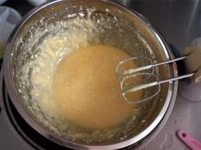 将打发好的蛋白坐入热水浴中，启动打蛋器，边打边倒入糖浆，搅打混合后，将融化了的黄油分两次加入，搅打融合。