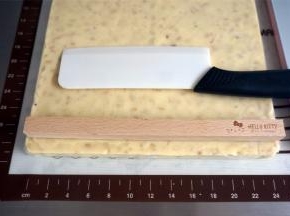 借助四件套中的方形木棍将牛轧糖切成均等宽度的长条。