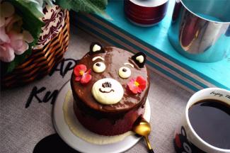 将巧克力甘纳许从慕斯中央开始一圈一圈覆盖慕斯表面，然后用刮刀稍微抹平。用淡奶油挤出熊本熊的眼睛，眼眉毛，嘴巴。最后用甘纳许点睛，画上小鼻子嘴巴，插上耳朵，完成。