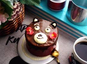 将巧克力甘纳许从慕斯中央开始一圈一圈覆盖慕斯表面，然后用刮刀稍微抹平。用淡奶油挤出熊本熊的眼睛，眼眉毛，嘴巴。最后用甘纳许点睛，画上小鼻子嘴巴，插上耳朵，完成。