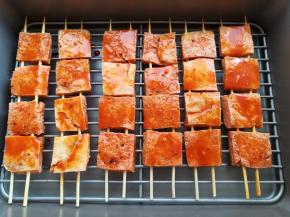 把串好的冻豆腐放到学厨的深烤盘晾网上，把多余的腌肉汁刷到冻豆腐上