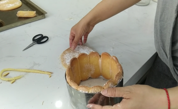 9.小心的将手指饼干脱模后摆入模具中裁去多余部分，圆形的蛋糕片裁剪的比慕斯圈/活底模具略小一些的尺寸，确保可以放入手指饼干围圈中。