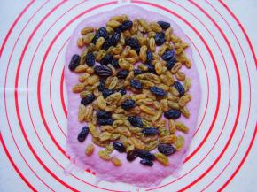 取一个面团擀成长条薄面片，末端压薄（利于封口）铺上提前泡软的葡萄干和黑加仑，轻轻按几下。