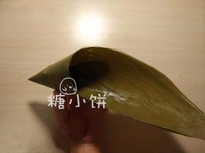 干粽叶用清水泡软，刷洗干净后煮5-10分钟，剪去硬梗部分。
取一片处理好的粽叶卷成漏洞形。