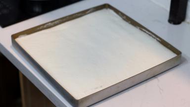 金盘内铺硅胶垫或者油布，将拌好的面糊倒入烤盘后再使用刮板将表面整理平整。