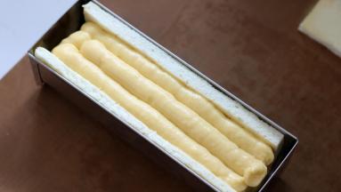 蛋糕片放入模具中摆好，先挤入模具一半高度的卡士达酱，放入冷冻成型的奶冻，再将剩余空间用卡士达酱填满。