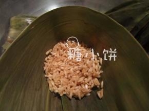 干粽叶提前用清水泡软，取一片叶片，从中间的位置对折出一个漏斗形。
如果要包大个一点，一片叶片不够长的话，可以两片交叠起来做。
在漏斗形中填入少许步骤3准备好的糯米，用勺子轻轻压实。