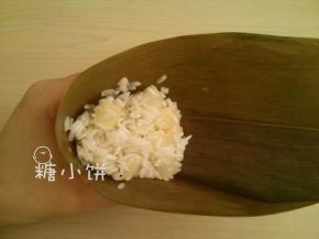 干粽叶用清水泡软，刷洗干净后煮5-10分钟，剪去硬梗部分。
取一片处理好的粽叶弯成漏洞形，填上拌好的米料