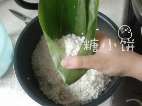 如图示把两边粽叶往中间压下去，这样包住不怕漏米。
正好也可以看出一个三角形的雏形了吧，嗯这一面也是个三角形样子的。
熟练了以后不用特意做这一步，此处只是为了分步图解更清楚一点。