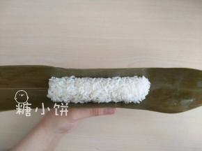 取一张粽叶，光面朝上（即接触糯米部分）弯出凹槽，中间填上糯米（如图）