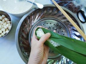 再添米，压平。
将粽叶两边向中心对折，叶子的长端部分窝过来盖住表面，再握紧包裹住整个粽子。