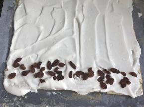 把蛋糕上的油纸拿去，抹上打发的奶油，再放入葡萄干