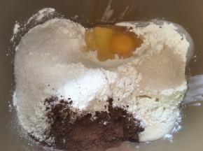 先来做可可面团，将高筋面粉，奶粉，炼乳，鸡蛋，可可粉，细砂糖跟酵母加入到面包桶内