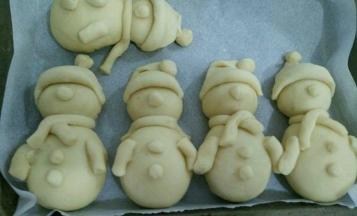 帽子做好后抹点水，沾到圣诞娃娃的脸部上方。然后搓三个小圆形面团做娃娃的鼻子和衣服扣子，最后再搓条形的面团做娃娃的手臂和围巾，一个娃娃就做好了，把剩下的四个娃娃也做好。