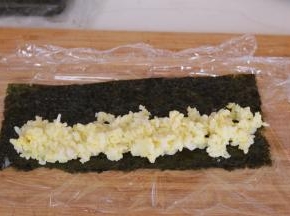 放入少许蛋黄米饭，借助保鲜膜卷起