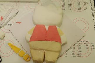 白色翻糖膏用力揉匀，擀成薄片，覆盖上KT的头部和手、脚，粉色翻糖膏做好衣服