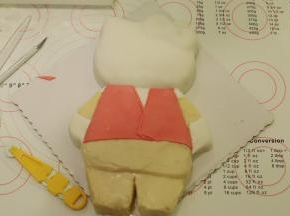 白色翻糖膏用力揉匀，擀成薄片，覆盖上KT的头部和手、脚，粉色翻糖膏做好衣服