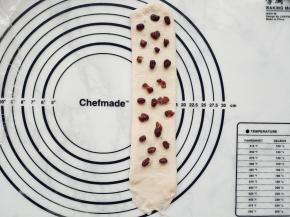 从中间开始分别向上向下擀开成长条形。在面团上铺上蜜豆，收尾处2厘米内不用铺。